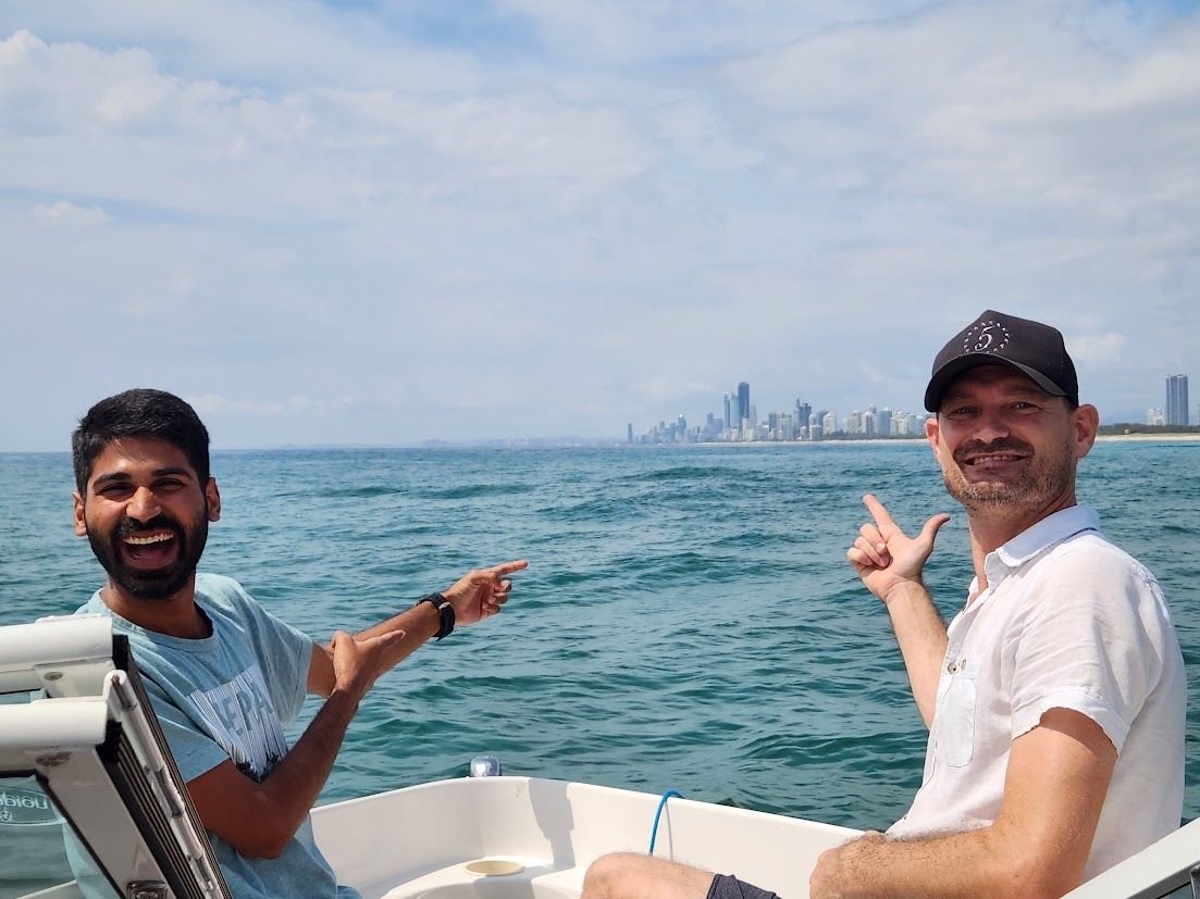 Ajay and a friend laughing on a boat with a city skyline behind them.