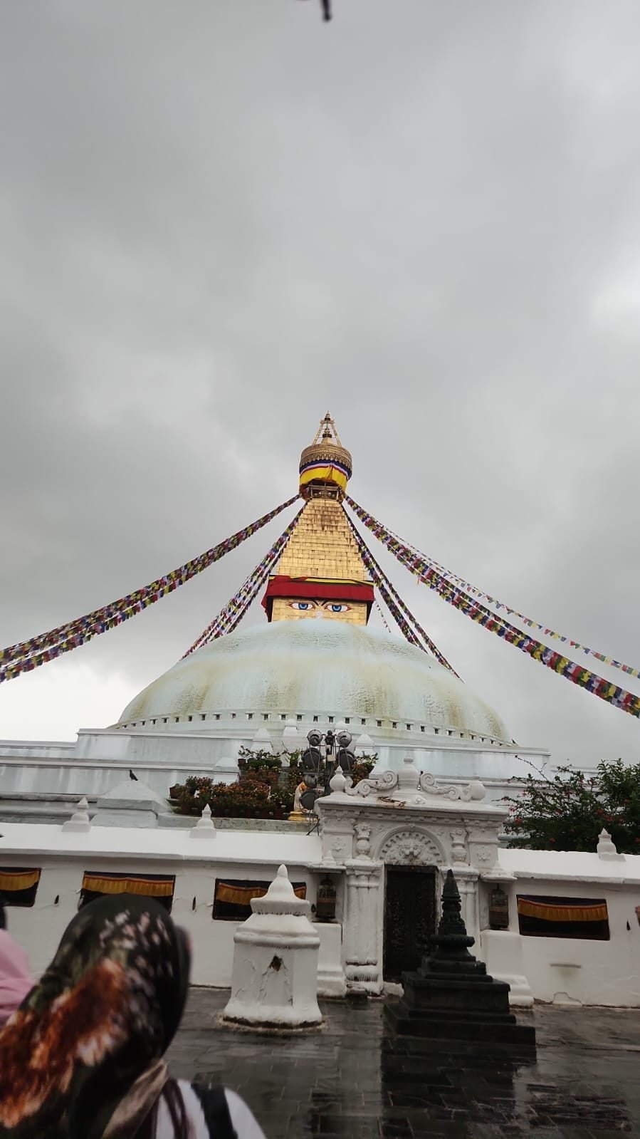 Boudhanath stupa under a grey monsoon sky, prayer flags running from the spire.