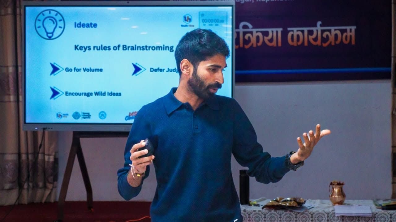 Ajay explaining the rules of brainstorming beside a projected slide at a programme in Nepal.