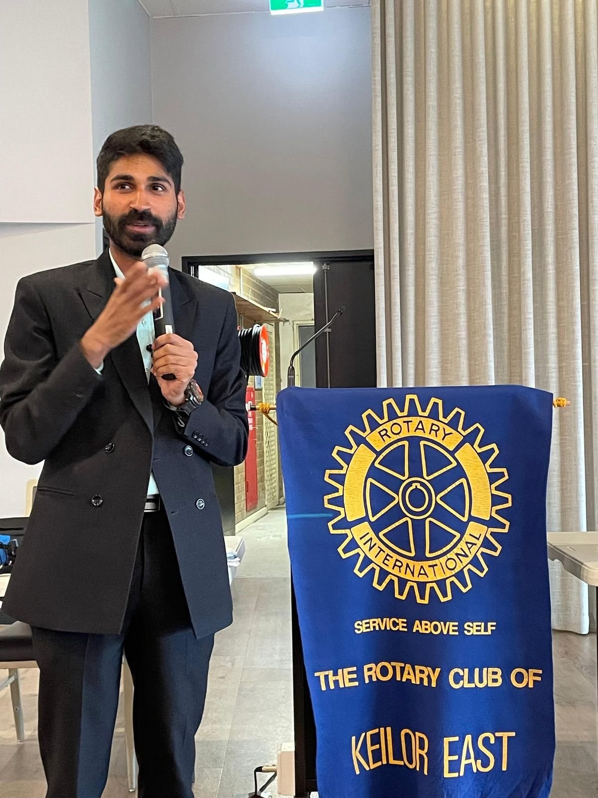 Ajay speaking beside a Rotary Club of Keilor East banner in Australia.