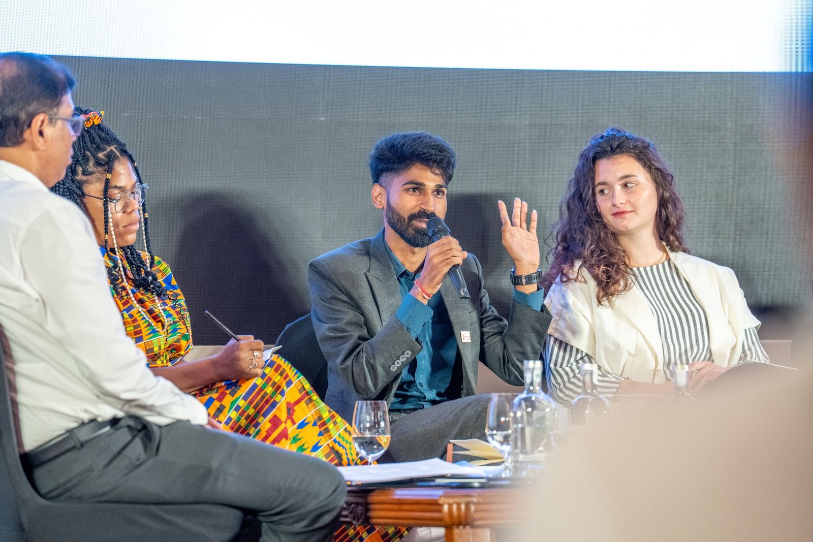Ajay on a panel of speakers seated in front of a large screen.