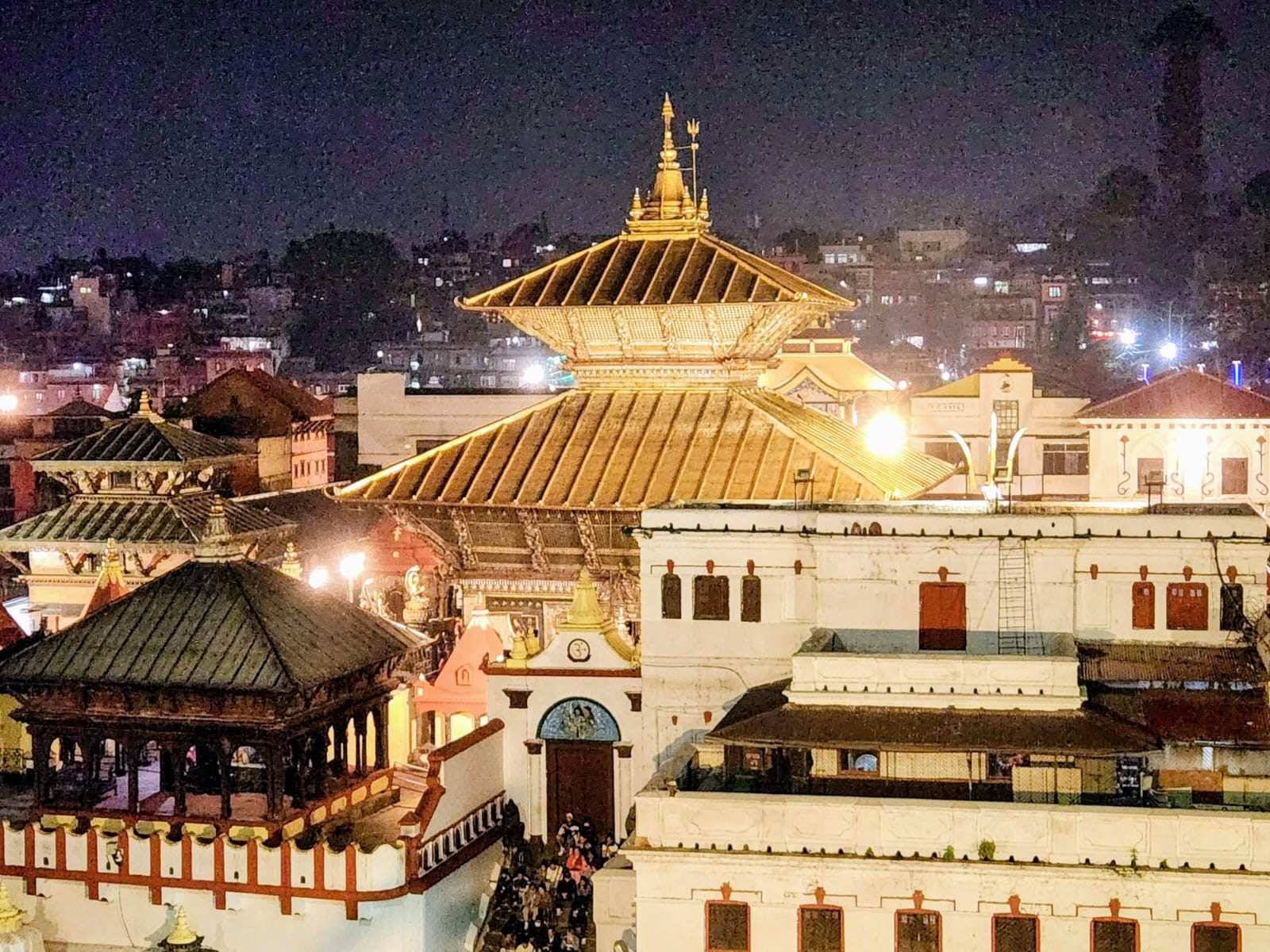The Pashupatinath temple complex lit at night, golden pagoda roofs rising above the courtyard.