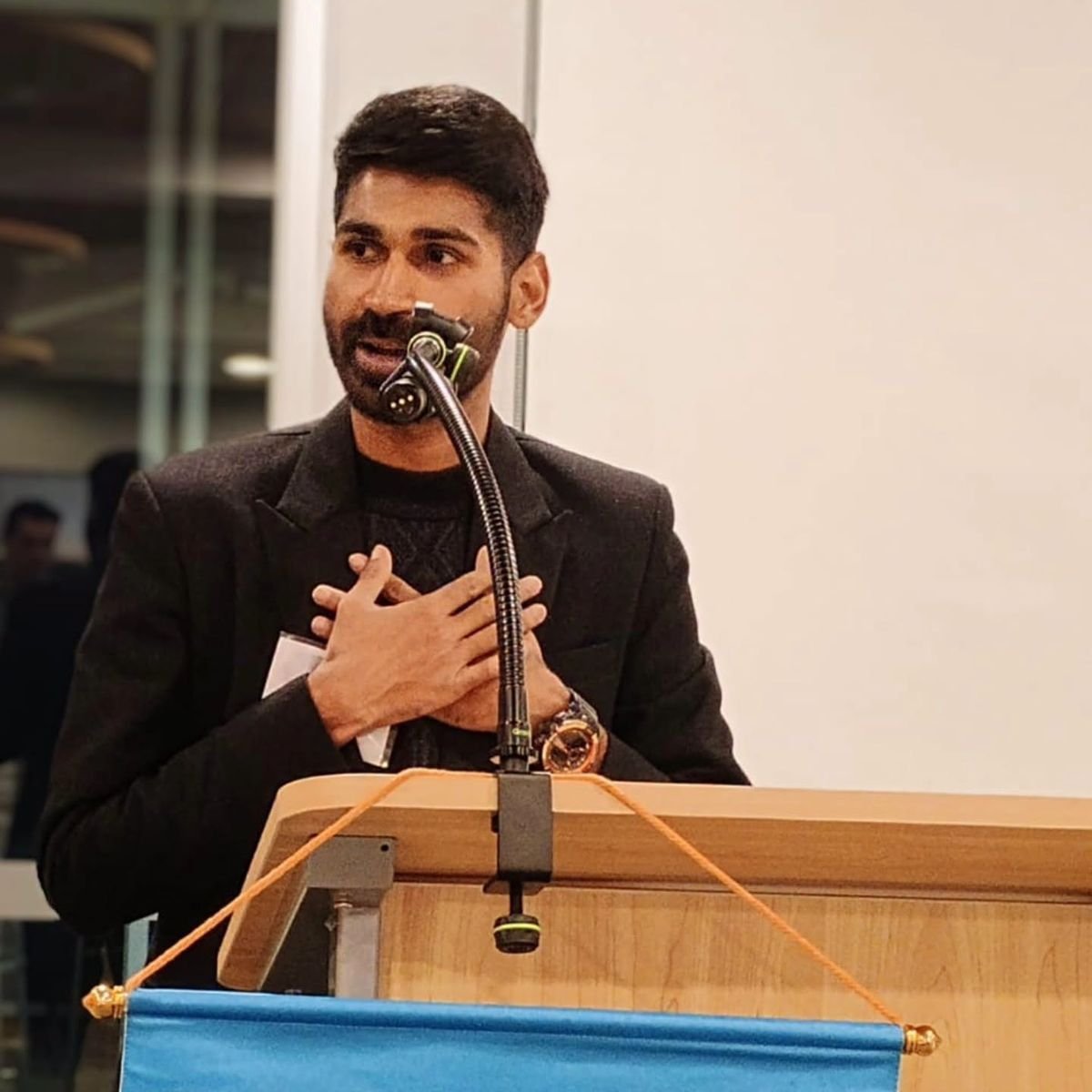 Ajay speaking at a lectern with a hand on his chest.