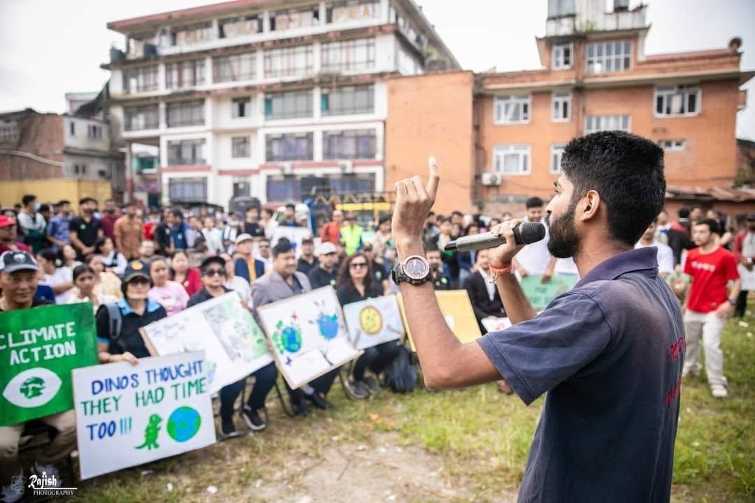Ajay addressing a large crowd of young people holding climate placards outdoors in Kathmandu.