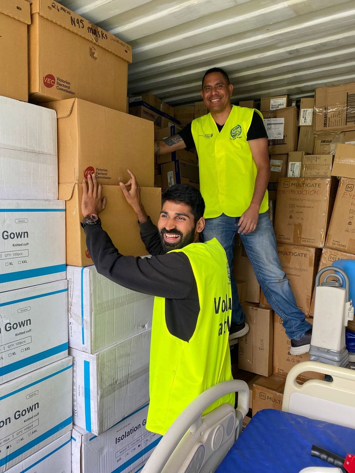 Ajay and another volunteer stacking supply boxes beside hospital equipment.
