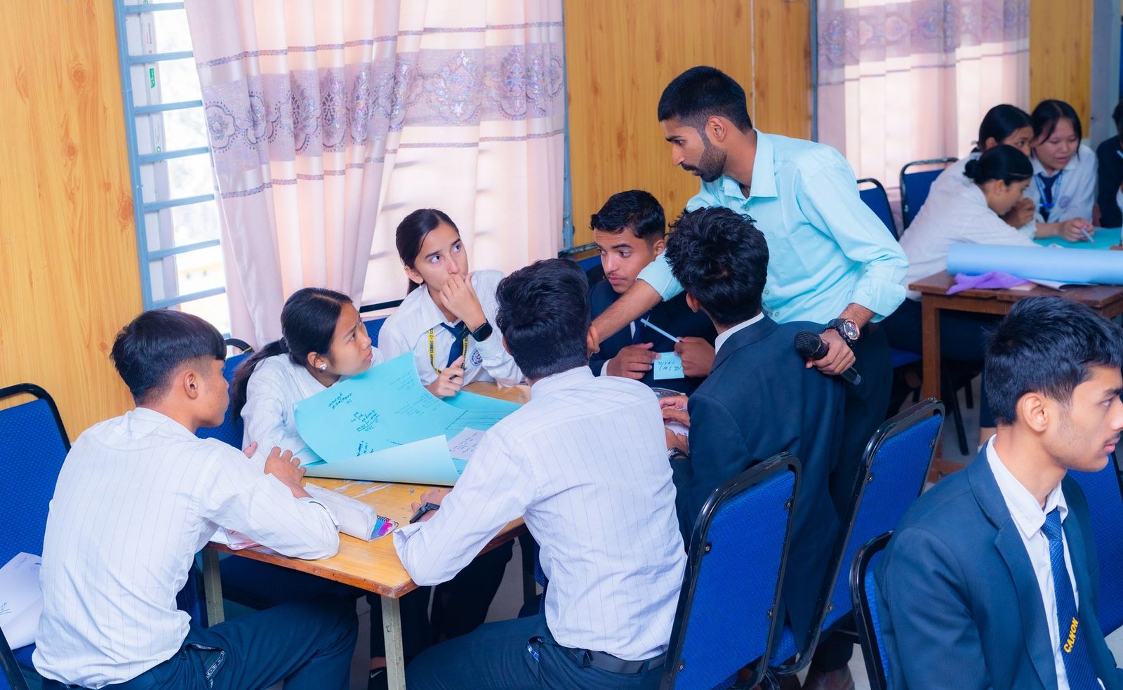 A classroom in Butwal with students clustered around desks in the middle of a design challenge.