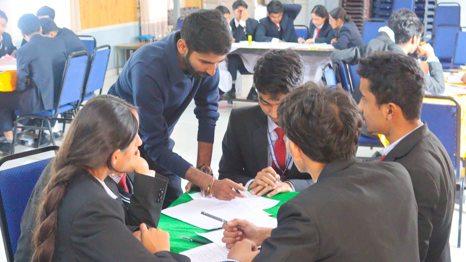 Ajay leaning over a table of students working through a design challenge.